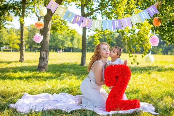 Alegre madre e hija divirtiéndose en el cumpleaños del niño en manta con decoraciones de papel en el parque —  Fotos de Stock