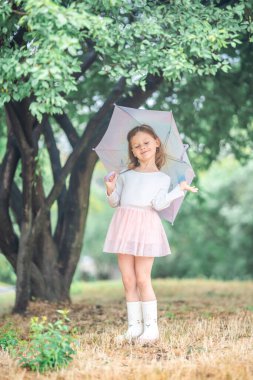 Küçük kız bir ağacın altında gözleri kapalı duruyor, şemsiyesini tutarken güzel bir şey hayal ediyor. Erken çocukluktaki şiirsel bir hayal ve hafif bir yağmur anı. Yüksek kalite fotoğraf