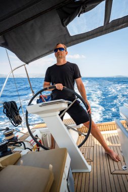 Hırvatistan yakınlarında yelkenli bir yatın dümeninde duran ve tekneyi açık denizde yüzdüren adam. Liderlik, kontrol, yelkencilik yaşam tarzı ve denizde özgürlük. Yüksek kalite fotoğraf