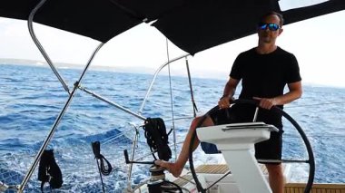 Hırvatistan yakınlarında yelkenli bir yatın dümeninde duran ve tekneyi açık denizde yüzdüren adam. Liderlik, kontrol, yelkencilik yaşam tarzı ve denizde özgürlük. Yüksek kalite 4k görüntü