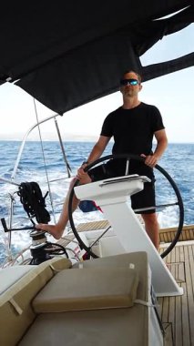 Hırvatistan yakınlarında yelkenli bir yatın dümeninde duran ve tekneyi açık denizde yüzdüren adam. Liderlik, kontrol, yelkencilik yaşam tarzı ve denizde özgürlük. Yüksek kalite 4k görüntü