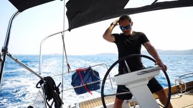 Hırvatistan yakınlarında yelkenli bir yatın dümeninde duran ve tekneyi açık denizde yüzdüren adam. Liderlik, kontrol, yelkencilik yaşam tarzı ve denizde özgürlük. Yüksek kalite 4k görüntü