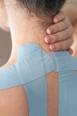 Kineziyoloji bandı boynuna ve omzuna uygulanan ve eliyle boynunu tutan genç bir kadının yakın görüntüsü. Modern rehabilitasyon yoluyla fizik tedavi ve kas iyileşmesi. 