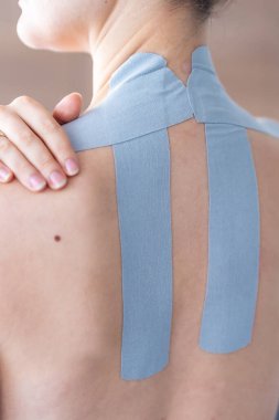 Omuz ve boyuna bantlanmış kineziyoloji bandı ve bantlanmış bölgede dinlenen bir kadın eli. Tedavi edici bant teknikleri ile ağrı kesici ve kendine bakım. Yüksek kalite fotoğraf
