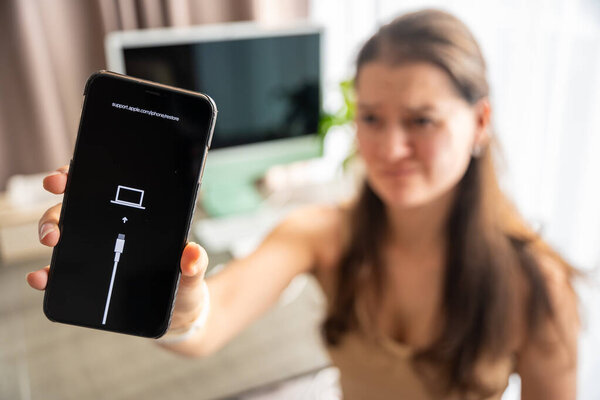 Prague, Czech republic - October 31, 2025: Frustrated woman showing iPhone in recovery mode with restore screen. Smartphone failure, data loss, and user reaction to unexpected technical problems