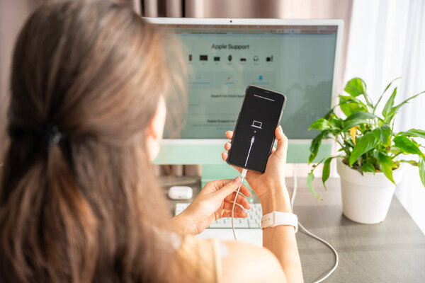 Prague, Czech republic - October 31, 2025: Woman trying to restore iPhone in recovery mode, browsing Apple Support website. Troubleshooting, data recovery, fixing smartphone issues with official help.