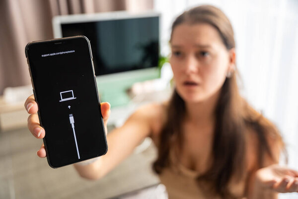 Prague, Czech republic - October 31, 2025: Frustrated woman showing iPhone in recovery mode with restore screen. Smartphone failure, data loss, and user reaction to unexpected technical problems