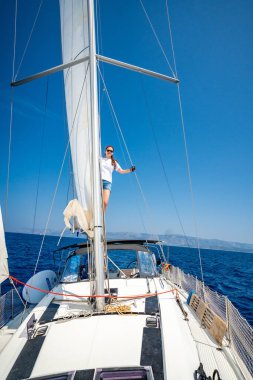 Açık deniz seyrüsefer sırasında yelkenli bir yatın direğinde duran genç bir kadın. Güç, özgürlük ve denizde korkusuz bir yaşam tarzı. Yüksek kalite fotoğraf