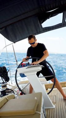 Hırvatistan yakınlarında yelkenli bir yatın dümeninde duran ve tekneyi açık denizde yüzdüren adam. Liderlik, kontrol, yelkencilik yaşam tarzı ve denizde özgürlük. Yüksek kalite 4k görüntü