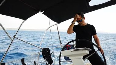 Hırvatistan yakınlarında yelkenli bir yatın dümeninde duran ve tekneyi açık denizde yüzdüren adam. Liderlik, kontrol, yelkencilik yaşam tarzı ve denizde özgürlük. Yüksek kalite 4k görüntü