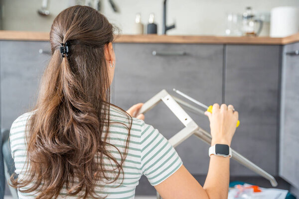 Молодую женщину видели сзади, собирающую стул с отвёртками на полу дома. Феминистская концепция женской независимости и сделать это самостоятельно сборка мебели. Высокое качество фото