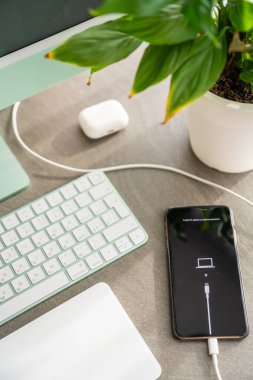 Prag, Çek Cumhuriyeti - 31 Ekim 2025: iPhone bilgisayara bağlı olarak masamda yatıyor. Akıllı telefon arızası, iOS kurtarma, yazılım çökmesi ve dijital sorun giderme, ev çalışma alanı.
