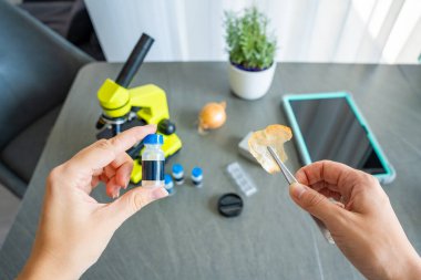 Bir insan, mikroskop altında incelemeden önce üzerinde daha fazla bilimsel malzeme bulunan bir soğan kabuğunu cımbızla küçük bir numune ile tutar. Bilim eğitimi kavramı ve çocuklar için ev deneyleri.