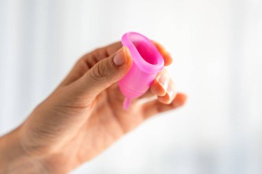 Ahşap masanın üzerinde duran bir kadının üzerinde duran pembe bir adet bardağının yakın çekimi. Kadınsal hijyen ürünü sıfır atık, konfor ve sürdürülebilir dönem bakımını teşvik ediyor