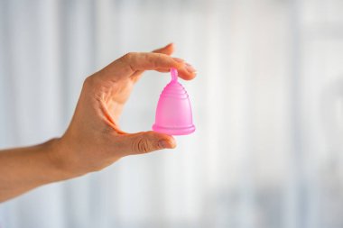 Ahşap masanın üzerinde duran bir kadının üzerinde duran pembe bir adet bardağının yakın çekimi. Kadınsal hijyen ürünü sıfır atık, konfor ve sürdürülebilir dönem bakımını teşvik ediyor