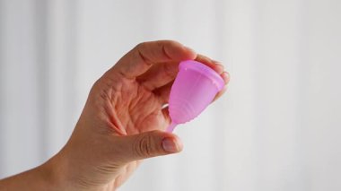 Ahşap masanın üzerinde duran bir kadının üzerinde duran pembe bir adet bardağının yakın çekimi. Kadınsal hijyen ürünü sıfır atık, konfor ve sürdürülebilir dönem bakımını teşvik ediyor