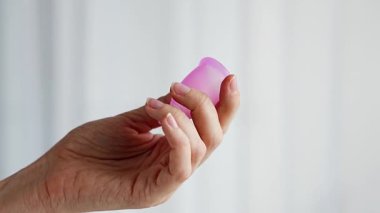 Ahşap masanın üzerinde duran bir kadının üzerinde duran pembe bir adet bardağının yakın çekimi. Kadınsal hijyen ürünü sıfır atık, konfor ve sürdürülebilir dönem bakımını teşvik ediyor