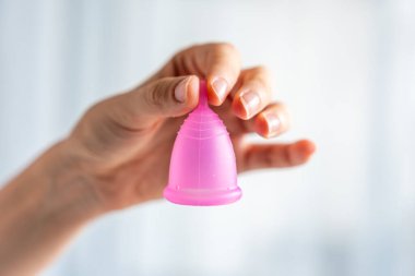 Ahşap masanın üzerinde duran bir kadının üzerinde duran pembe bir adet bardağının yakın çekimi. Kadınsal hijyen ürünü sıfır atık, konfor ve sürdürülebilir dönem bakımını teşvik ediyor