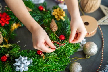 Tatil teknesi etkinliği sırasında süslü bir Noel çelengi tutan küçük ellerin yakın çekimi. Şenlik yaratıcılığının ve çocukluk döneminin ev geleneklerine olan sembolik katılımı