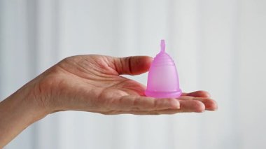 Ahşap masanın üzerinde duran bir kadının üzerinde duran pembe bir adet bardağının yakın çekimi. Kadınsal hijyen ürünü sıfır atık, konfor ve sürdürülebilir dönem bakımını teşvik ediyor