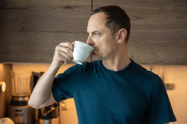 Modern bir mutfakta çay içen bir adam. Sabah içeceği ritüeli.