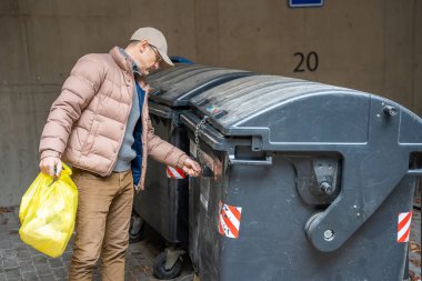 Çöpü sarı plastik bir torbayla çöpe atan bir adam. Atık yönetimi ve günlük sorumluluklar.