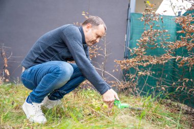 Bahçesinde yabani otları elleriyle çeken bir adam. Bahar bahçesi hazırlığının ve çevreci yaşam tarzının sembolü