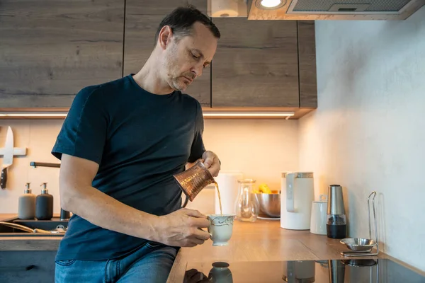 Modern bir mutfakta bir bardağa süt döken bir adam. Günlük ev rutini.