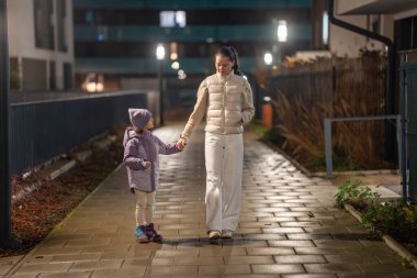Yağmurdan sonra ebeveyn ve kızının yerleşim alanlarında yürüdüğü şehir akşam manzarası. Islak kaldırım, rahat kıyafetler ve aile bakımı..