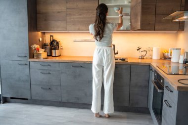 Evdeki mutfak dolabında bulaşık yıkayan bir kadın. Gerçek hayatta günlük ev organizasyonu ve ev içi depolama rutini.