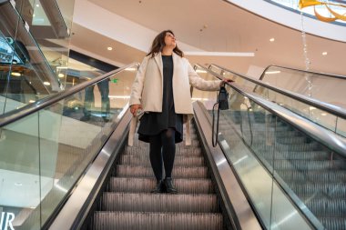 Her gün alışveriş merkezinde yürüyen merdivene binen bir kadın. Modern tüketici yaşam tarzı, kentsel rutin ve kamu ticaret sahasında günlük hareket.