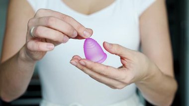 Elinde pembe bir regl fincanı tutan bir kadının kullanıma hazırlandığı yakın plan. Sürdürülebilir hijyen, kişisel bakım ve çevre dostu dönem ürünlerinin teşvik edilmesi