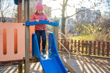 Baharda şehir parkında kayan küçük bir kız. Çocukluk, açık hava aktivitesi, mevsimsel oyun ve gerçek hayatta şehir ortamında günlük boş zaman..