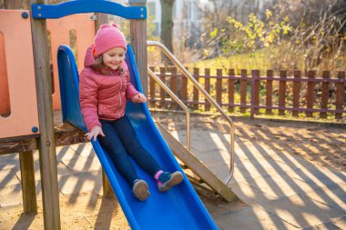 Baharda şehir parkında kayan küçük bir kız. Çocukluk, açık hava aktivitesi, mevsimsel oyun ve gerçek hayatta şehir ortamında günlük boş zaman..