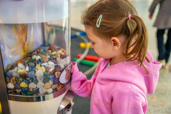 Mücevher otomatının yanında duran küçük bir kız alışveriş merkezinde rastgele bir taş bekliyor. Çocukluk merakı anı, aile eğlence deneyimi gerçek hayatta ticari çevrede.