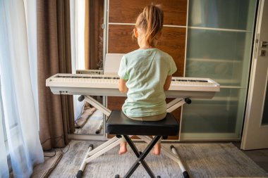 Küçük kız piyanonun başında oturuyor ve evde müzik çalıyor. İfade ve dikkatli duruş. Çocukluk müzik eğitimi, yaratıcı gelişme, konsantrasyon, disiplin ve sakin öğrenme ortamı.