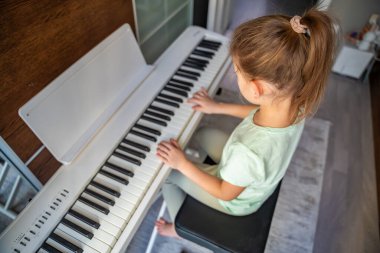 Küçük kız piyanonun başında oturuyor ve evde müzik çalıyor. İfade ve dikkatli duruş. Çocukluk müzik eğitimi, yaratıcı gelişme, konsantrasyon, disiplin ve sakin öğrenme ortamı.