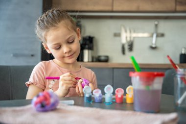 Mutfakta yumurtaları süslerken gülümseyen genç bir kız. Paskalya geleneklerine neşeli bir katılım ve aile bağları. Mevsimsel yaratıcılık, evde festival geleneği ruhu.