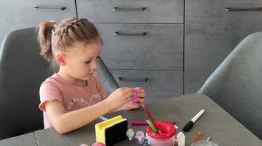 Küçük kız evde otururken Paskalya yumurtalarını renkli çıkartmalarla süslüyor. Yaratıcı Paskalya aktivitesi, basit yumurta süsleme tekniği ve kapalı alanda neşeli tatil hazırlığı.