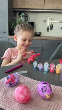 Paskalya yumurtalarını süslerken elini kırmızı boyayla boyayan küçük bir kız. Yaratıcı Paskalya aktivitesi, çocukluk merakı ve kapalı alanda eğlenceli tatil hazırlığı..