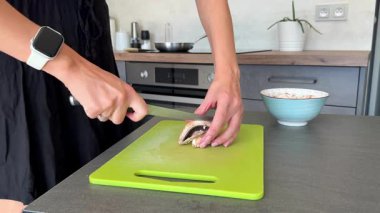 Ev mutfağında yemek hazırlarken kadın ellerinin bıçakla mantar doğraması. Malzeme işleme adımı, ev yapımı pizza pişirme rutini ve evde günlük yemek hazırlığı.