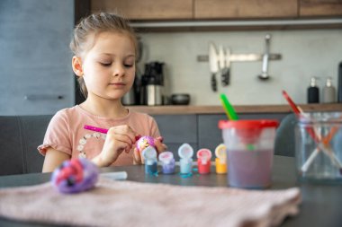Mutfakta yumurtaları süslerken gülümseyen genç bir kız. Paskalya geleneklerine neşeli bir katılım ve aile bağları. Mevsimsel yaratıcılık, evde festival geleneği ruhu.