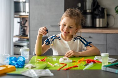 Küçük bir kristalle test tüpü tutan ve dikkatlice incelenen genç bir kız laboratuvar masasında sonuç veriyor. Bilimsel gözlem, kristal büyüme deneyi yoluyla pratik BTMM öğrenmesi