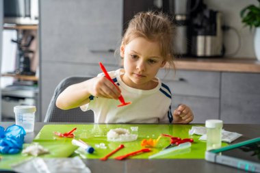 Genç kız cımbızla kristali dikkatlice tutuyor ve ev bilimi deneyi sırasında inceliyor. Erken dönem STEM eğitimi ve kimya öğreniminde hassas çalışma ve analitik düşünme