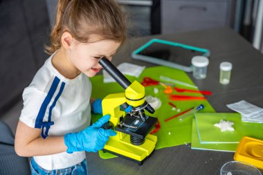 Kristal yapısını mikroskopla inceleyen genç bir kız. Büyüyen kristallerle yapılan deney sırasında. Erken STEM eğitimi ve merakı, bilimsel keşifleri yurtiçinde yürütüyor