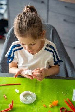 Yıldız şeklindeki kristali tutan genç bir kız evdeki laboratuvar masasında yüzeyini ve dokusunu dikkatlice inceliyor. Kristal yetiştirme deneyi ve bilimsel keşifler üzerine erken STEM eğitimi