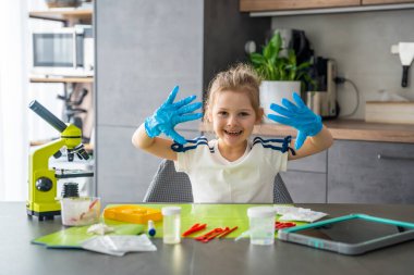 Kristal yetiştirme deneyi sırasında mikroskop ve bilim malzemeleriyle laboratuvar masasında koruyucu eldiven takan gülümseyen kız.