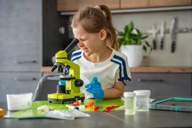 Kristal yapısını mikroskopla inceleyen genç bir kız. Büyüyen kristallerle yapılan deney sırasında. Erken STEM eğitimi ve merakı, bilimsel keşifleri yurtiçinde yürütüyor