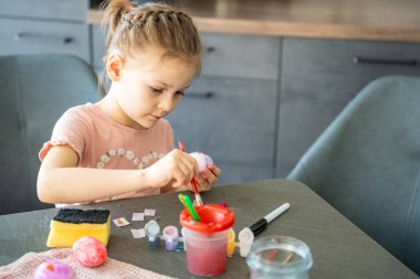 Paskalya yumurtalarını fırça ve renkli boyalarla boyayan çocuk. Yaratıcı Paskalya zanaatı süreci, festival hazırlıkları ve kapalı alanlarda yapılan etkinlikler.