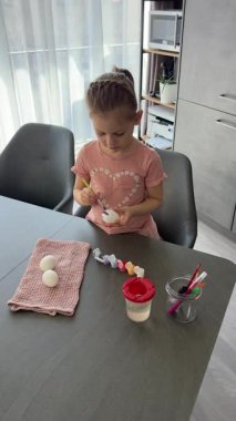 Paskalya yumurtaları üzerinde çalışırken gülümseyen bir çocuk. Sanatsal ifade yoluyla neşe, rahatlık ve gelenek yakalıyor..